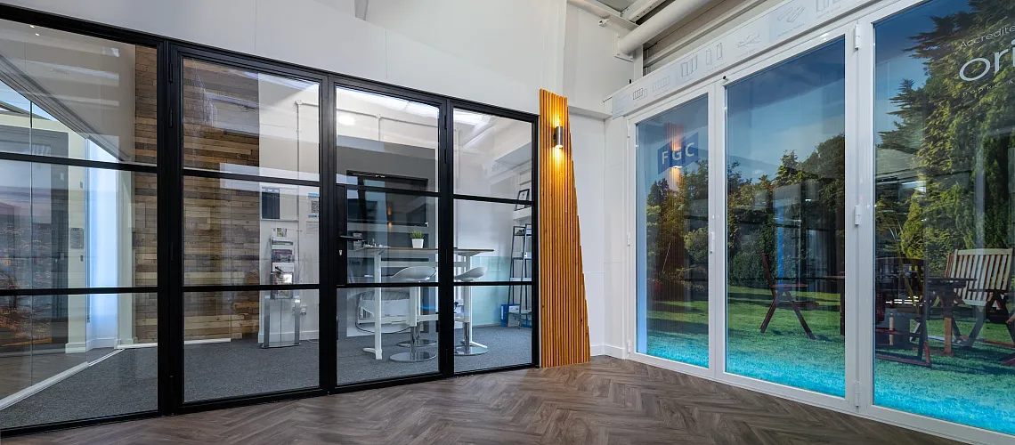 Showroom with herringbone floor, displaying a black steel-look screen and a white bifold door