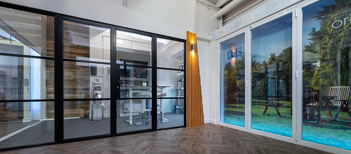 Showroom with herringbone floor, displaying a black steel-look screen and a white bifold door