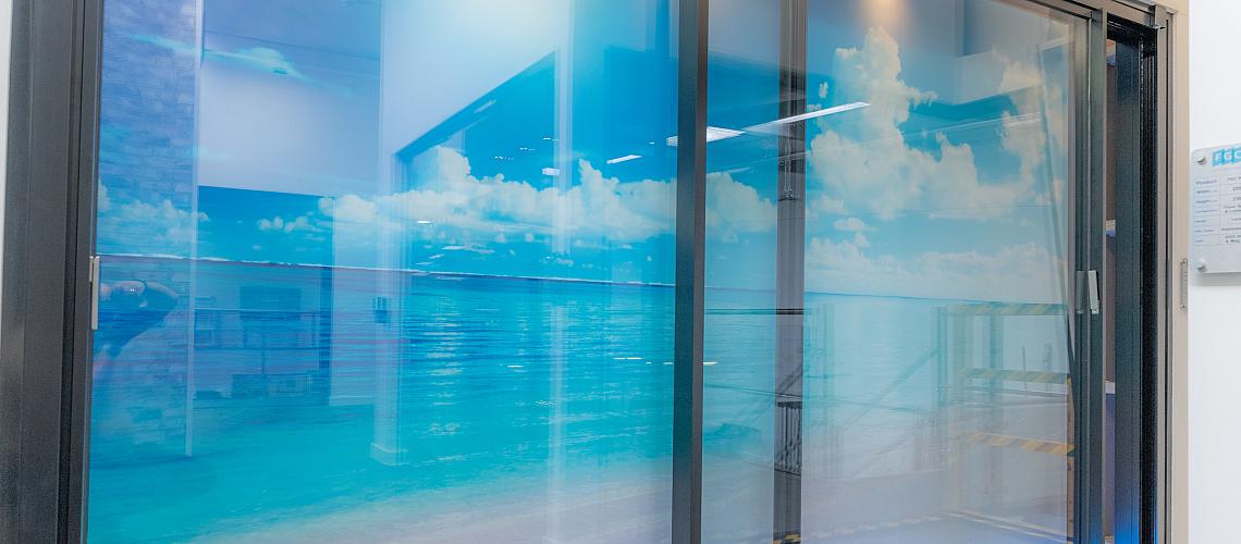 A large black sliding door display in a showroom, featuring a bright, backlit graphic of a tropical ocean scene
