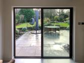 A closed dark brown slimline sliding door viewed from inside, showing the slim central meeting stile and garden view.