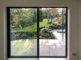 Interior view of a dark brown slimline sliding door with one panel open, showing a seamless view of the patio and garden.