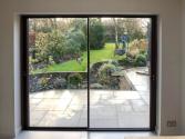Interior view from a second slimline sliding door, open to the garden patio with a round glass table and hanging chair.