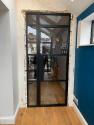 A black heritage aluminium single door with a side panel, installed in an unfinished wall, viewed from the inside