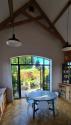 Interior of a rustic kitchen with vaulted ceiling. Black steel-look arched doors are open, showing a sunny garden and patio