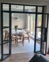 Black steel-look double doors fully open, providing a wide view of the dining room and patio doors beyond