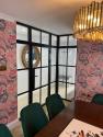 Black steel-look French doors set in a white wall, with one door open, leading from the patio into a bright kitchen