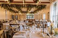 Elegant wedding reception hall with decorated tables. Tall, black steel-look windows and doors line the room