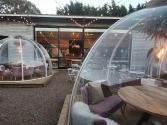 Outdoor patio at dusk with lit dining igloos. Large black steel-look windows on the commercial building behind