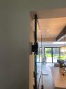 An angled view of an open black steel-look internal door showing the handle, leading from a hallway into a living room.