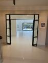 Open black steel-look double doors viewed from a hallway, leading into a large, bright room with white tiled floors