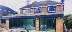 Brick house extension under construction, showing two large dark grey sliding doors and matching upstairs windows
