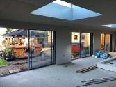 Interior of a room being built, with three black sliding doors looking out to a garden that has a gazebo and hot tub.
