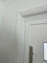 Close-up of the top corner of the closed white front door. Shows the white frame and the upper part of the long vertical handle