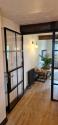 Angled view of an open black steel-look door with a bronze handle, showing the living room beyond