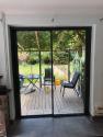Interior view of a closed black slimline sliding door looking out onto a wooden deck with patio furniture
