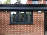 A dark grey three-panel casement window set into a red brick wall, below a dark flat roof