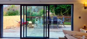 Black Origin sliding door with the left panel slid open, viewed from inside a room under construction, looking onto a deck