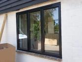 A newly installed black three-panel Origin window set into a white brick wall, with construction materials visible nearby
