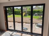 Interior view of closed four-panel black Origin bifold doors. The room and outside garden are both under construction