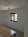 A small, two-panel black Origin casement window with a handle, set in the white wall of a room under construction