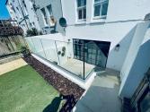 High-angle view of a sunken patio with black steel-look doors, enclosed by a frameless glass balustrade