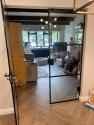 Closed black steel-look double doors with horizontal bars. View from a herringbone floor hallway into a modern dining room.