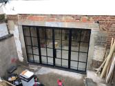 Interior view of closed four-panel black steel-look doors. The surrounding room is under construction with exposed beams