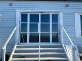 Exterior view of a closed white steel-look bifold door set, at the top of white stairs on a blue clad building