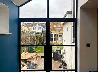 Interior view of black heritage double doors with a large, shaped apex window above, looking out onto a back garden