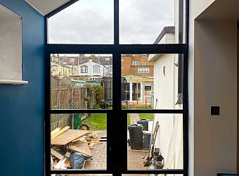 Interior view of black heritage double doors with a large, shaped apex window above, looking out onto a back garden