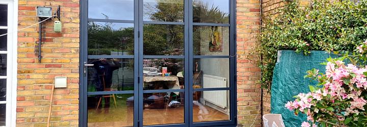 Interior view of closed black steel-look three-panel bifold doors, looking out onto a back garden