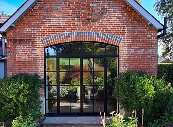 Exterior view of a red brick building with the black steel-look arched doors fully closed. A sunny patio is in the foreground