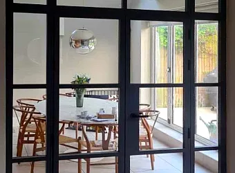 Closed black steel-look double doors with side and top panels, looking into a modern dining room with a round table