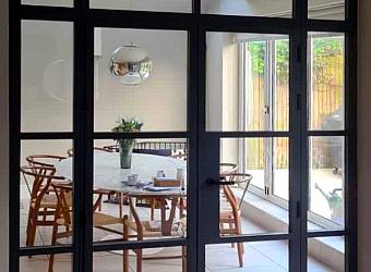 Closed black steel-look double doors with side and top panels, looking into a modern dining room with a round table