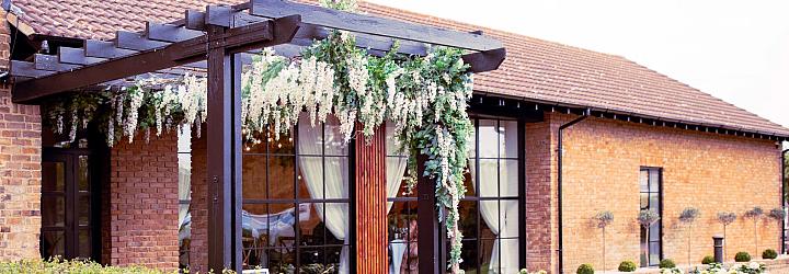 Exterior of a brick venue with a black, flower-draped pergola. Large, black steel-look windows and doors are set into the wall