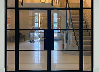 Closed black steel-look double doors with side panels, viewed from a hallway, looking into another hall with a staircase