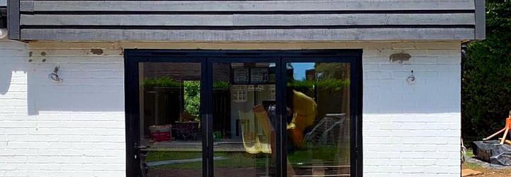 Exterior view of black three-panel Origin bifold doors set in a white brick and black clad wall during renovation.