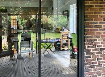 Exterior view of the black slimline sliding door set in a brick wall, showing reflections of the garden on the glass