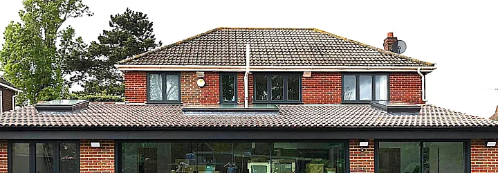 Straight-on view of a brick extension with large dark grey sliding doors, a matching side window, and upstairs windows