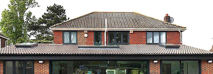 Straight-on view of a brick extension with large dark grey sliding doors, a matching side window, and upstairs windows