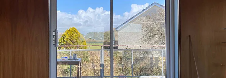 White two-panel Origin sliding door, closed, in a wood-panelled room. View shows a sunny balcony and a neighbouring house