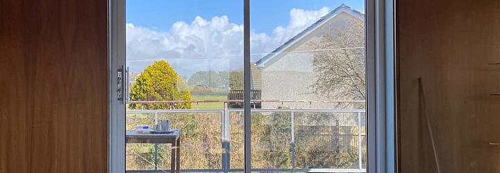 White two-panel Origin sliding door, closed, in a wood-panelled room. View shows a sunny balcony and a neighbouring house