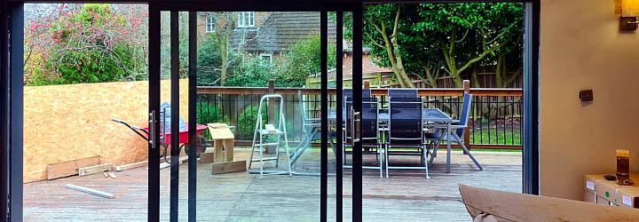 Black Origin sliding door with the left panel slid open, viewed from inside a room under construction, looking onto a deck
