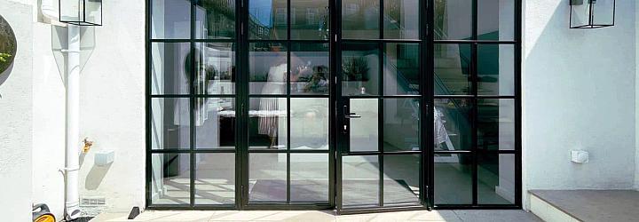 Exterior view of closed black steel-look French doors with side panels, set in a white wall on a sunny patio