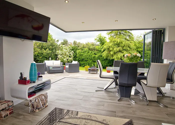 Modern dining room with bifold doors fully open, showing a seamless transition to an outdoor patio with garden furniture
