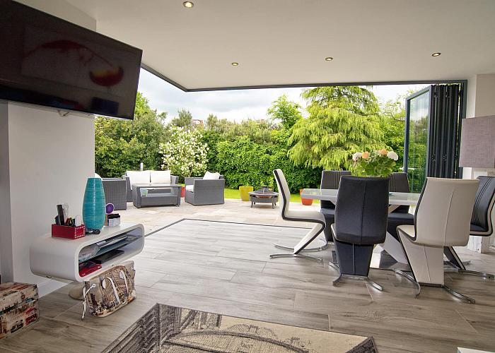 Modern dining room with bifold doors fully open, showing a seamless transition to an outdoor patio with garden furniture