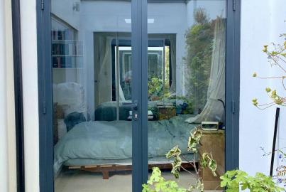 Closed, dark grey two-panel Origin OB-49 bifold doors, viewed from outside, looking into a modern bedroom