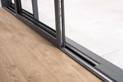 Close-up of the floor track and base of a dark grey Origin OS-44 sliding door, showing the transition from wood floor to tile