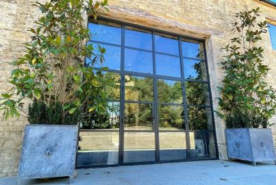 Exterior of closed black steel-replacement French doors with a grid, set in a stone wall under a large wood lintel