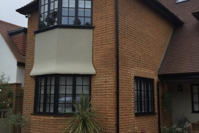 A red brick house with black steel-replacement windows, featuring a large two-story bay window with grid panes